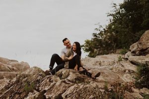engaged couple laugh while sitting on rocks in great falls park