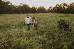 engaged couple walk in tall grass holding hands