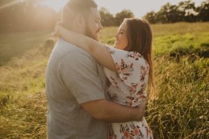 woman reaches up and hugs fiance during golden sunset