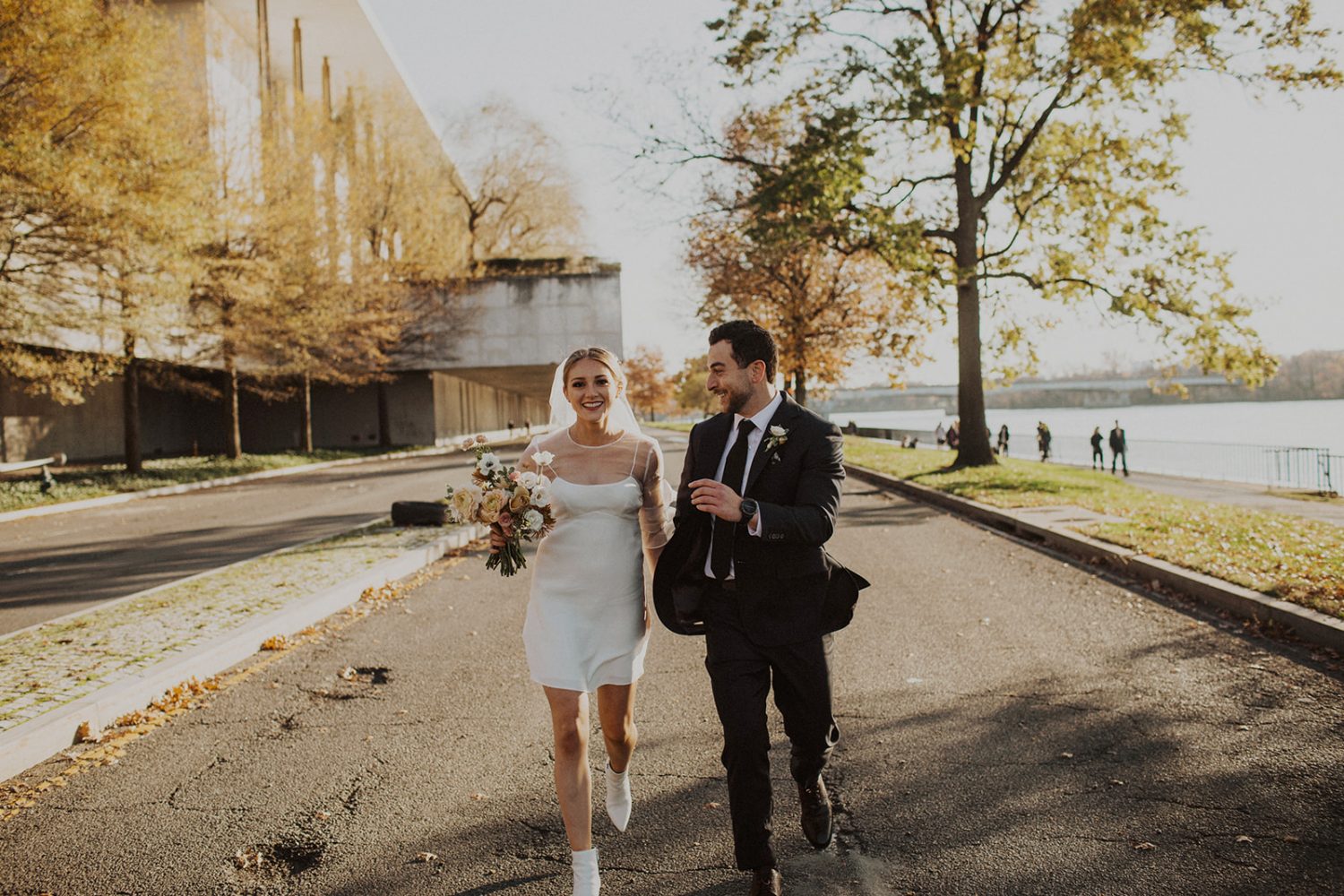 Bride and groom walk along the river holding bouquet 