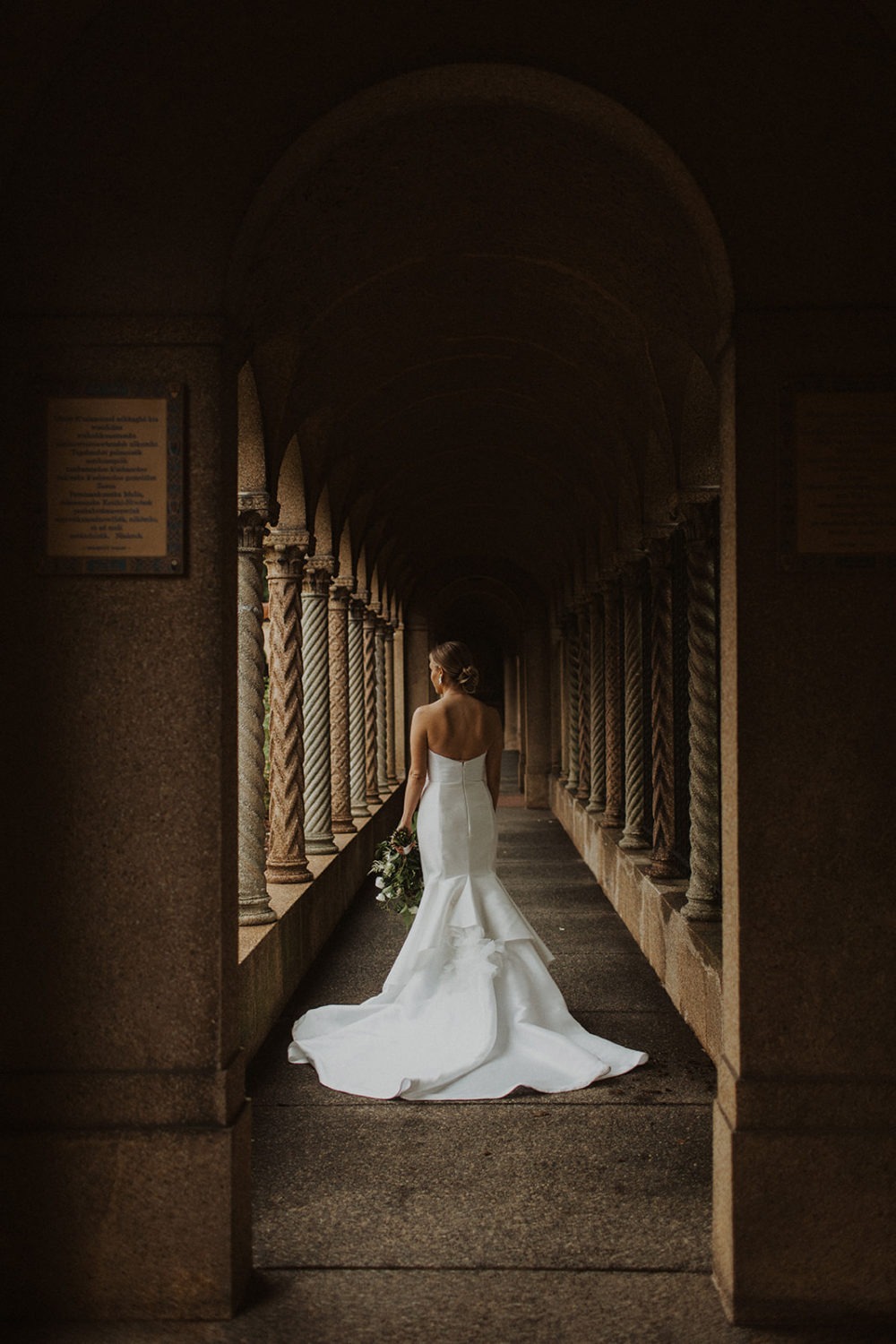 Bride stands beside columns in wedding dress