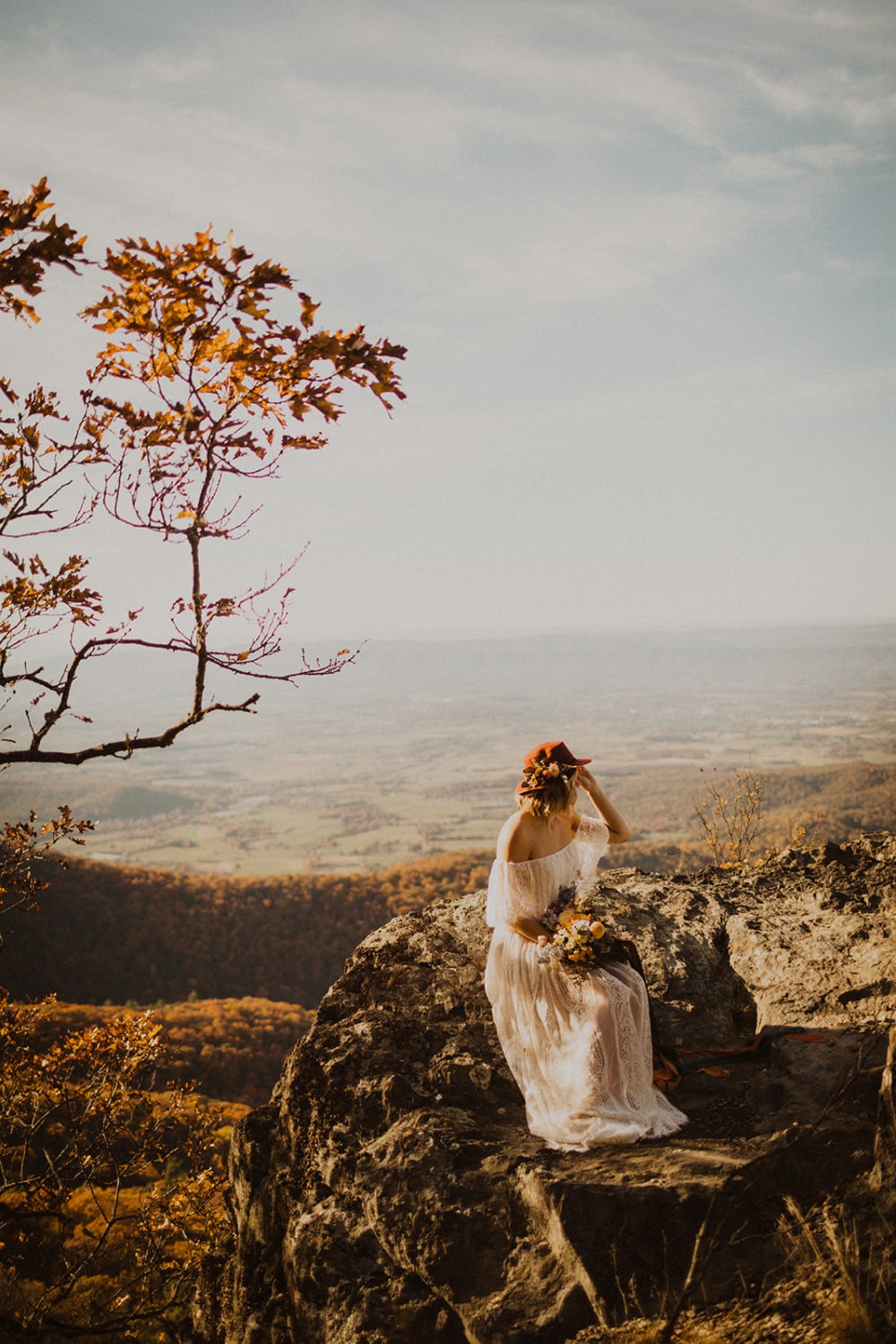 Bride sits on hill holding wedding bouquet at Shenandoah National Park