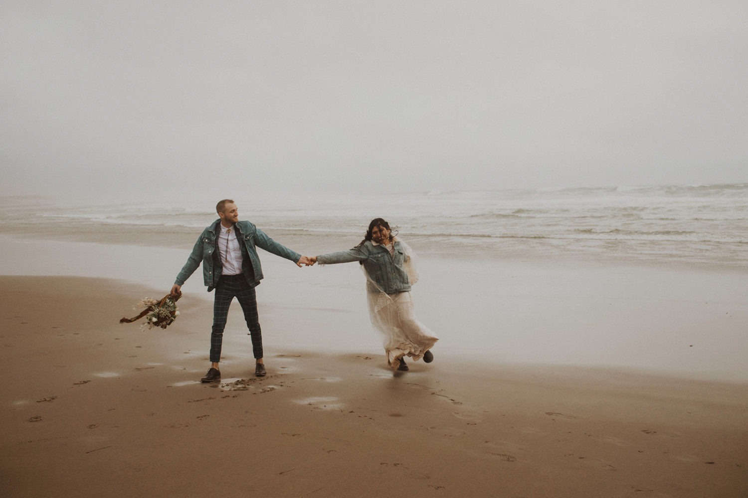 Couple holds hands on beach at rainy elopement