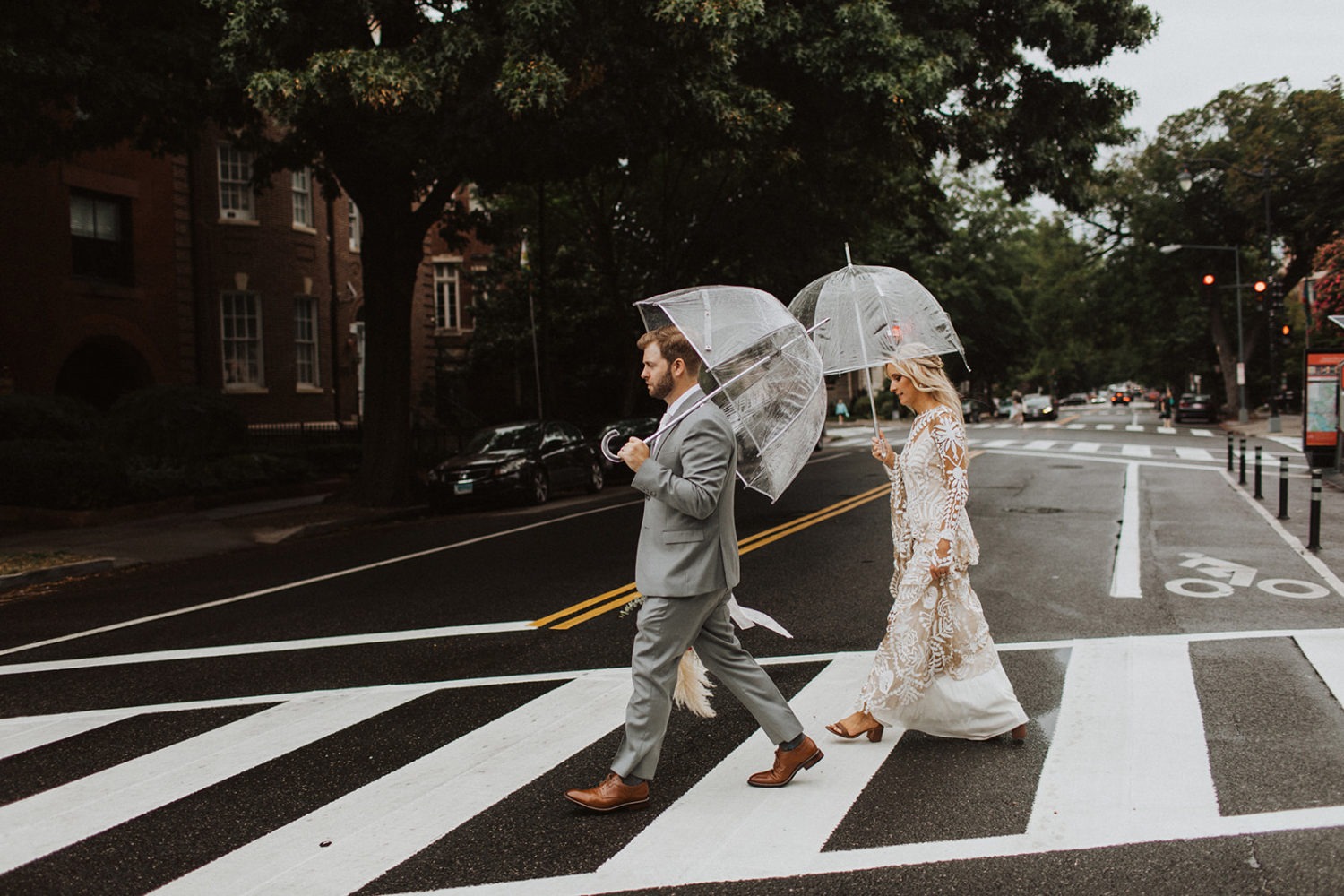 Couple crosses street holding umbrellas at rainy wedding day