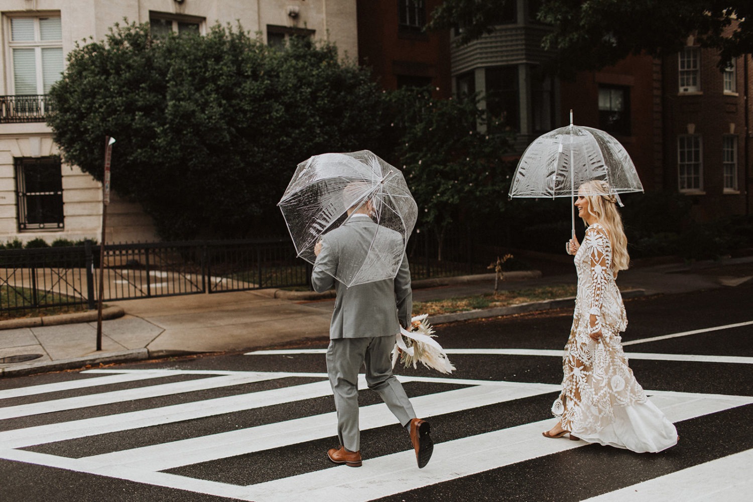 Couple walks under clear umbrellas at rainy wedding day