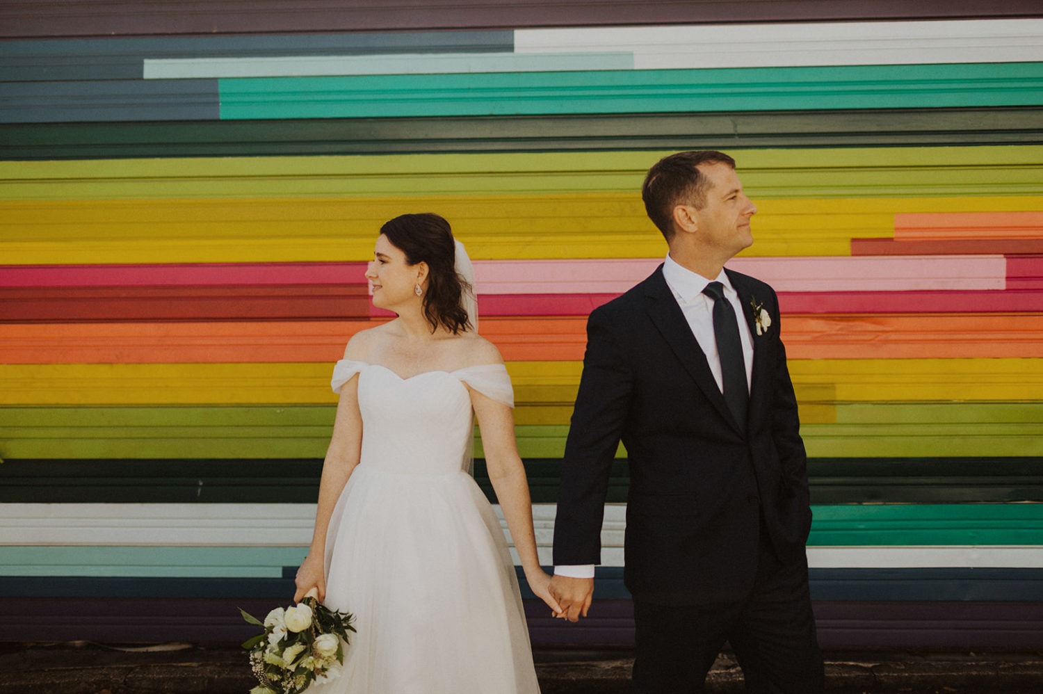 Couple stands in front of rainbow wall at full-day elopement