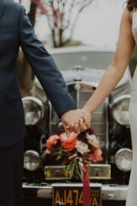 Couple holds hands in front of vintage car at postponed wedding day