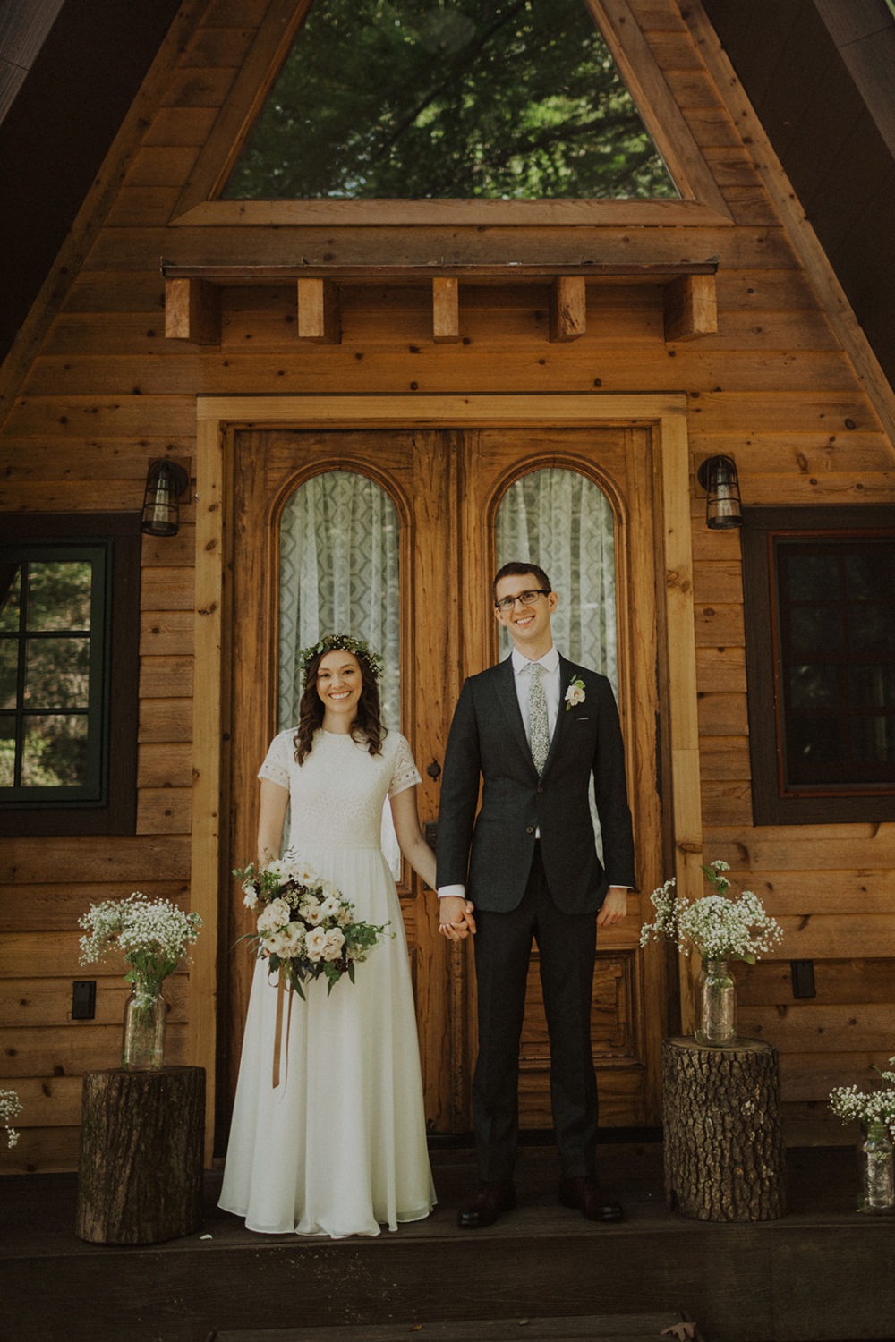 Couple stands holding hands outside of a-frame cabin at adventure elopement