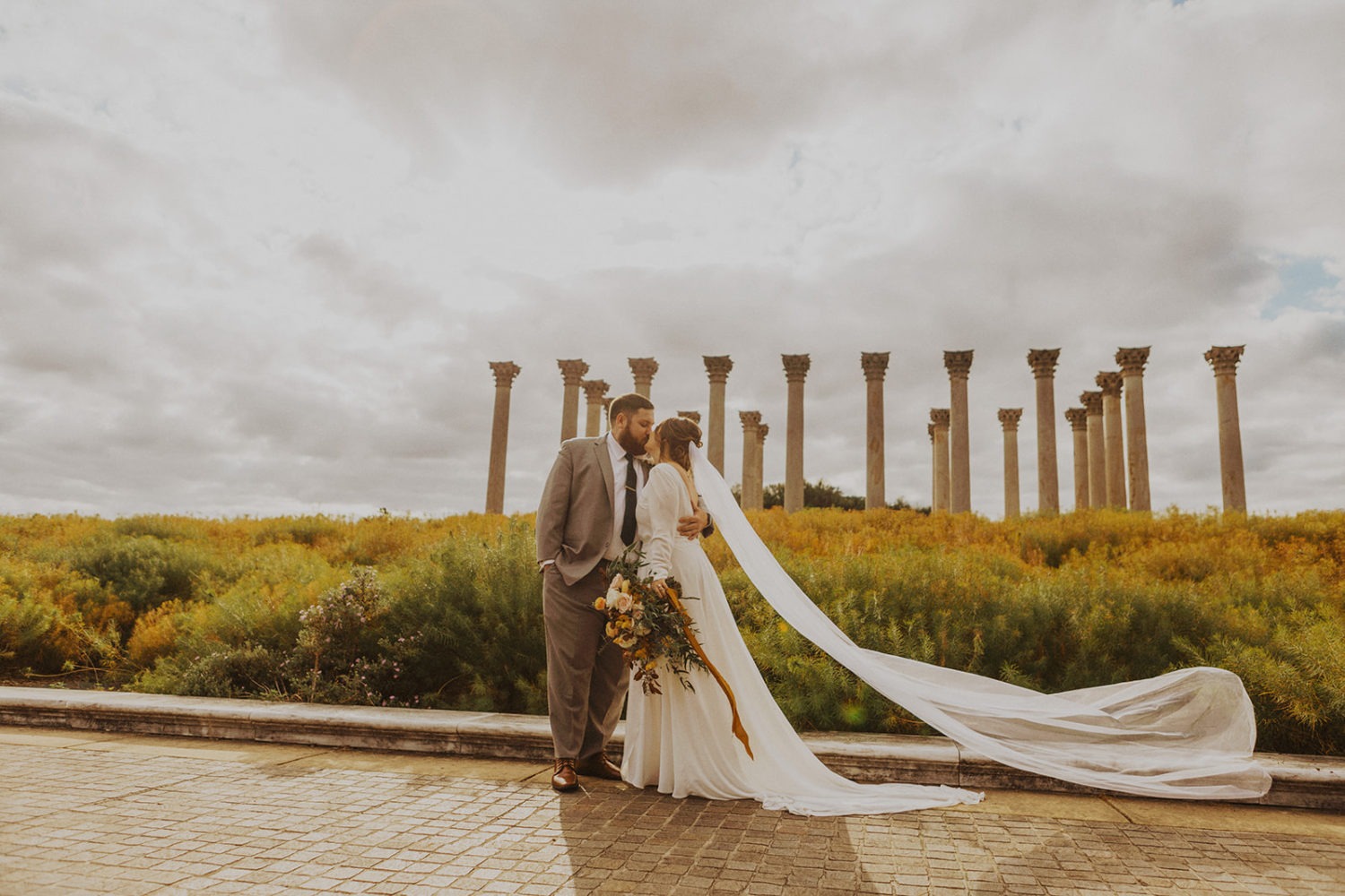 Couple kisses in front of columns at Arboretum wedding