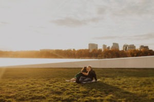 Couple kisses sitting on grass at Washington DC sunset engagement session