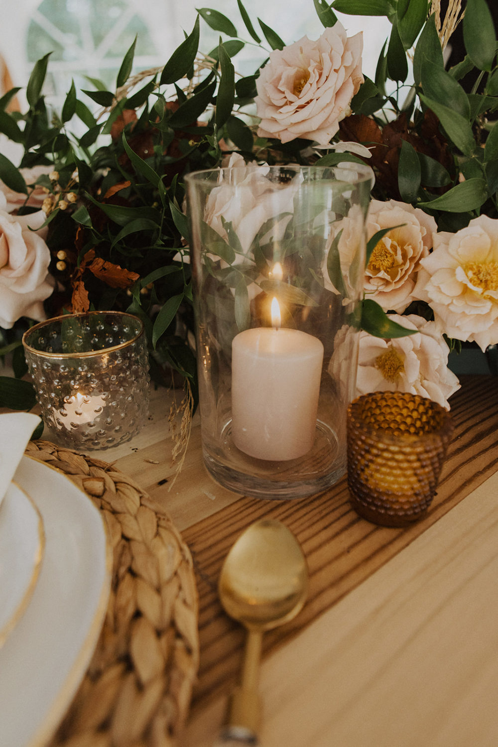 Lit candle in vase beside wedding flowers on reception table
