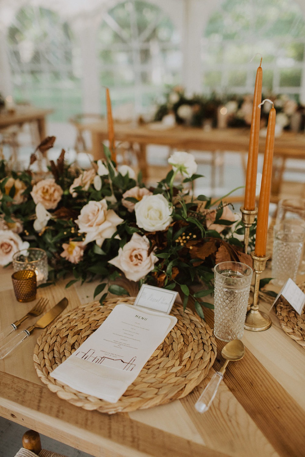 A menu, candles, and greenery decorate wedding reception table