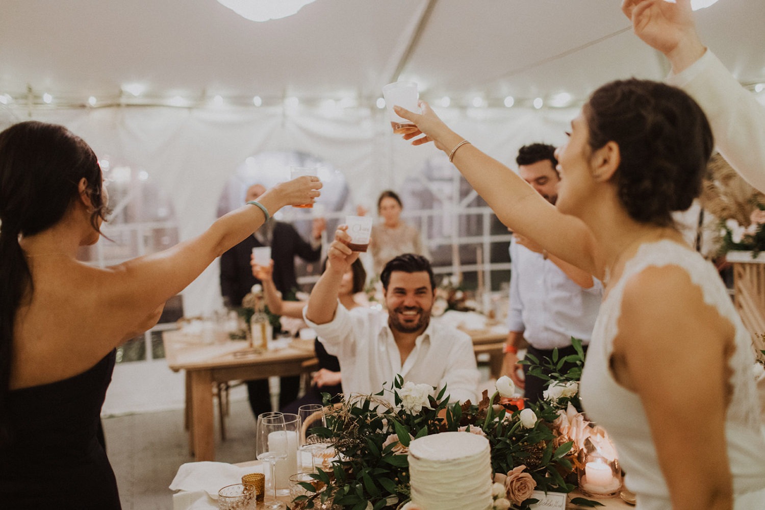 Couple cheers with guests at in reception tent