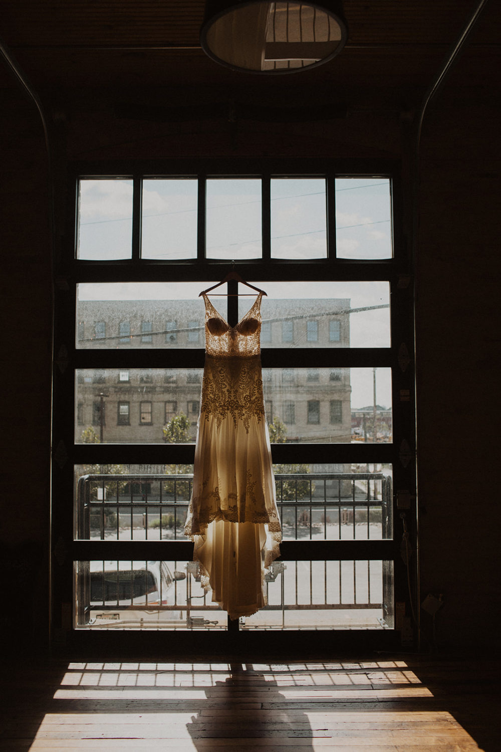 Wedding dress hangs on window with light shining through it
