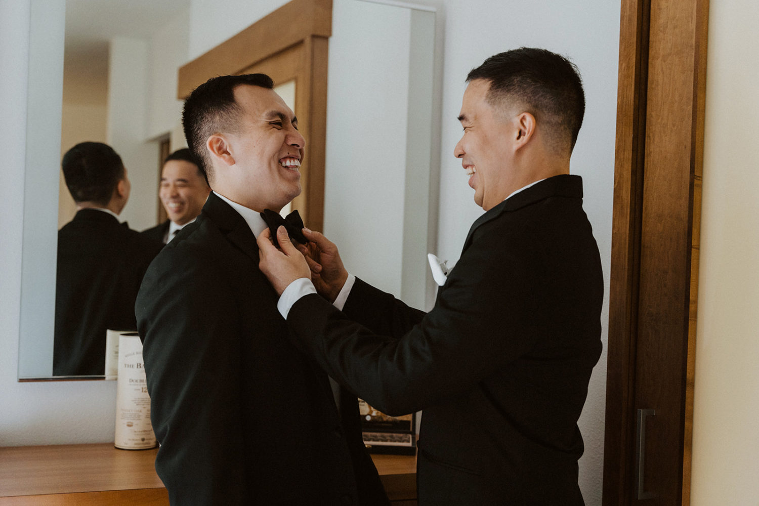 Groom has help tying his bow tie while getting ready on the wedding morning 