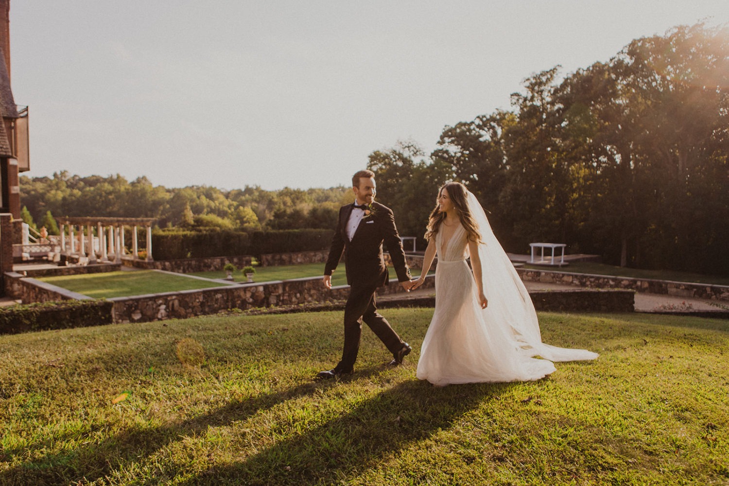 Couple walks across lawn of wedding venue while being capture by wedding videographer