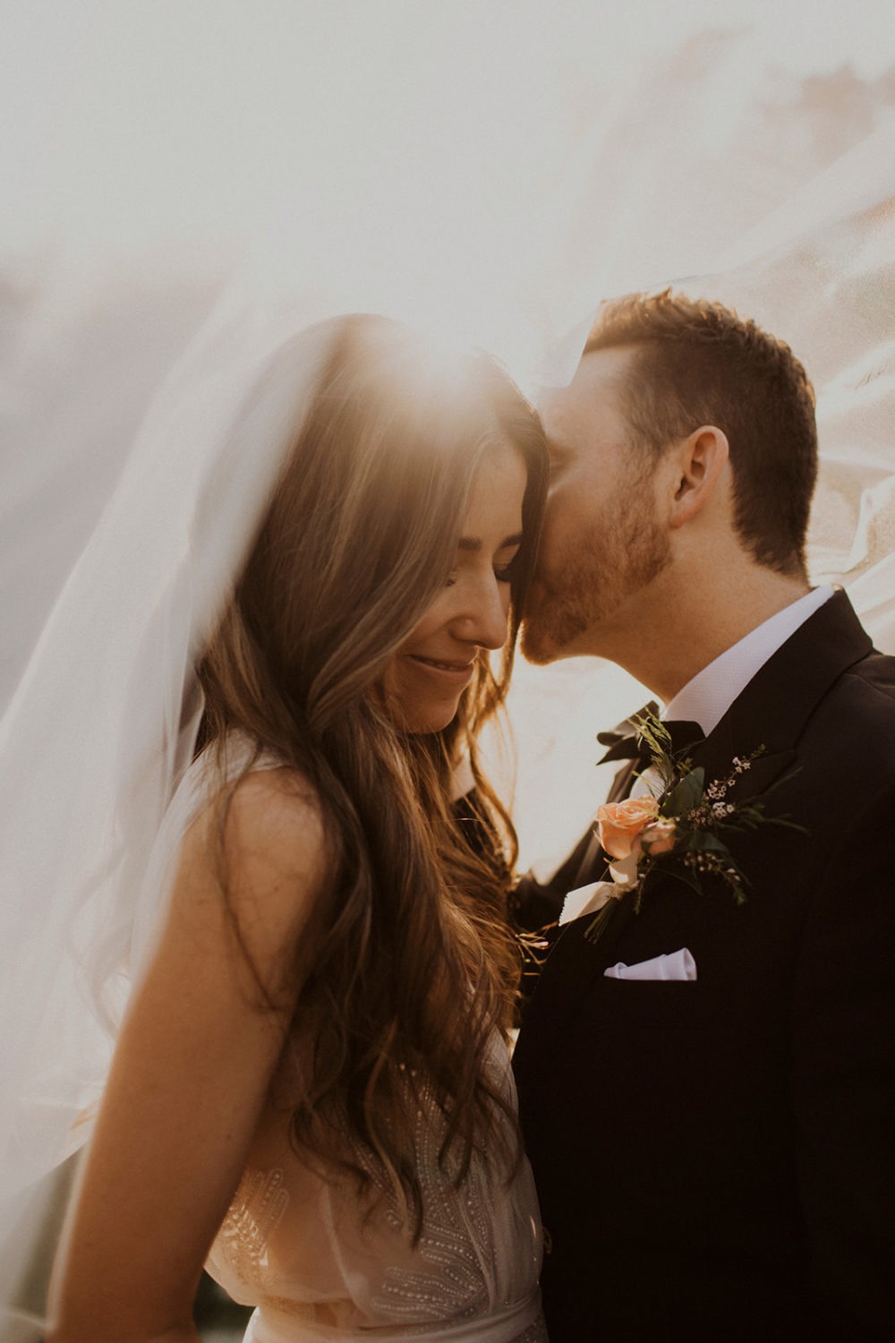 Couple kisses under veil while captured by wedding videographer