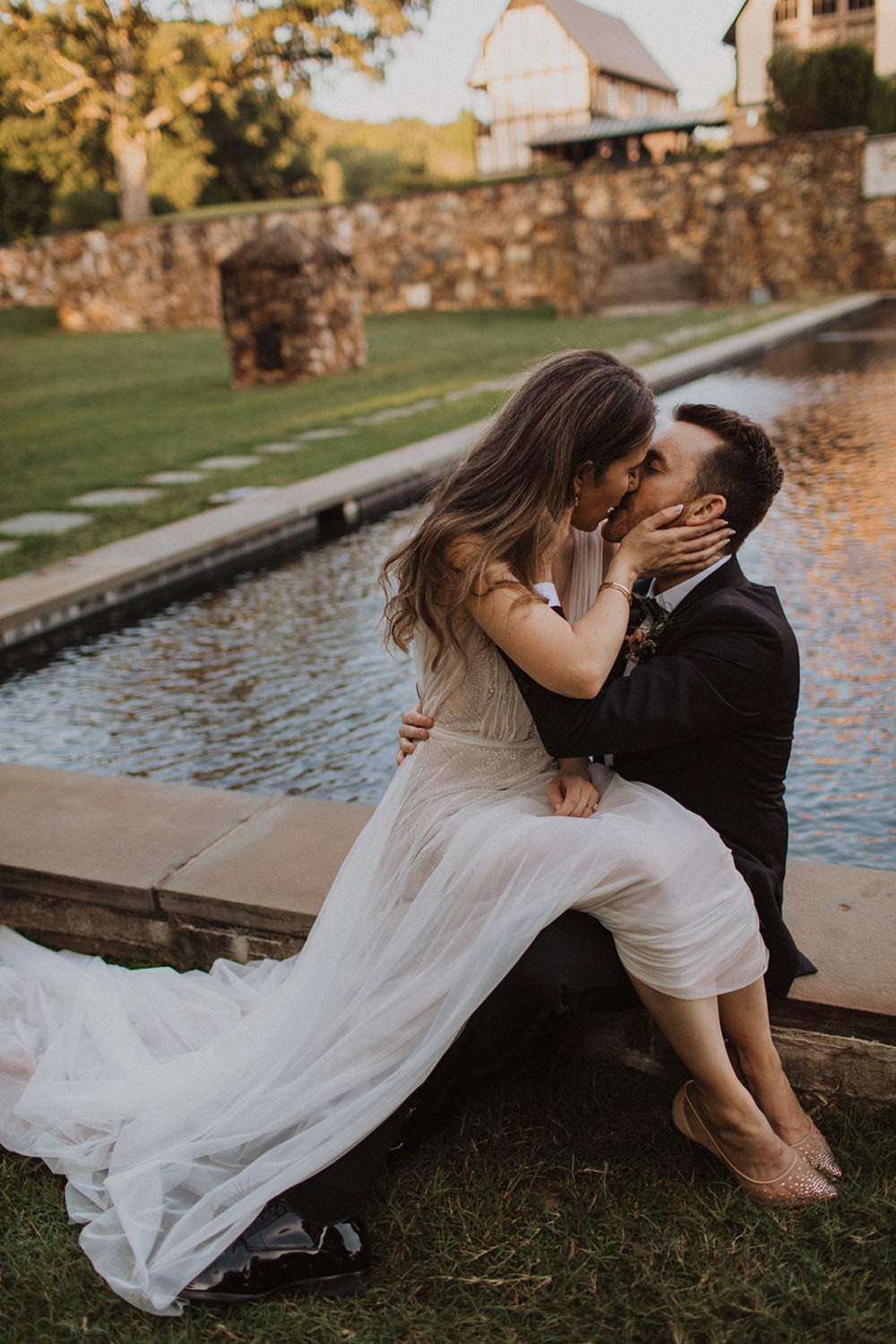 Bride sits on groom's lap and kisses outside by pool