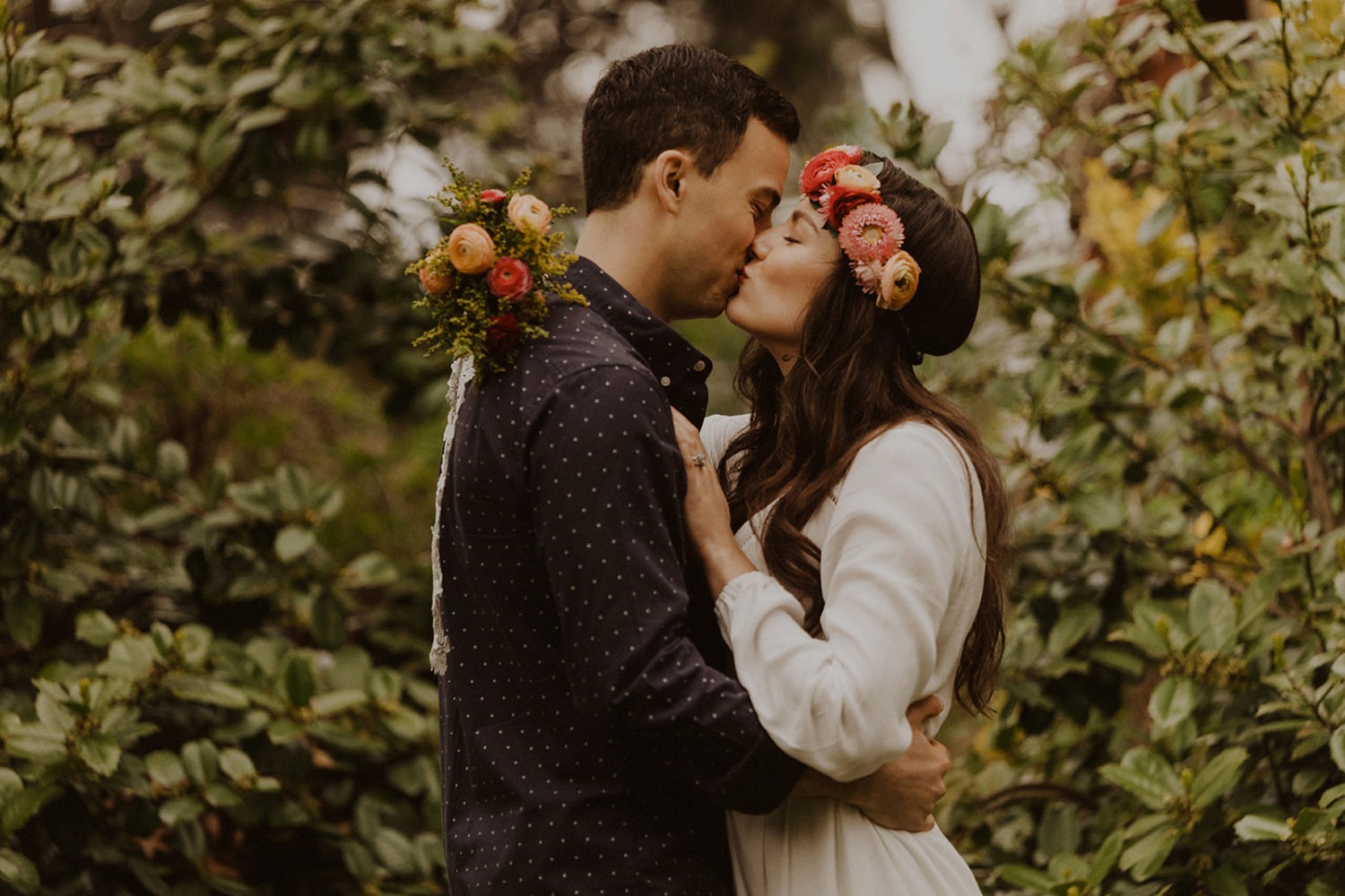 Couple kisses while holding spring wedding flowers