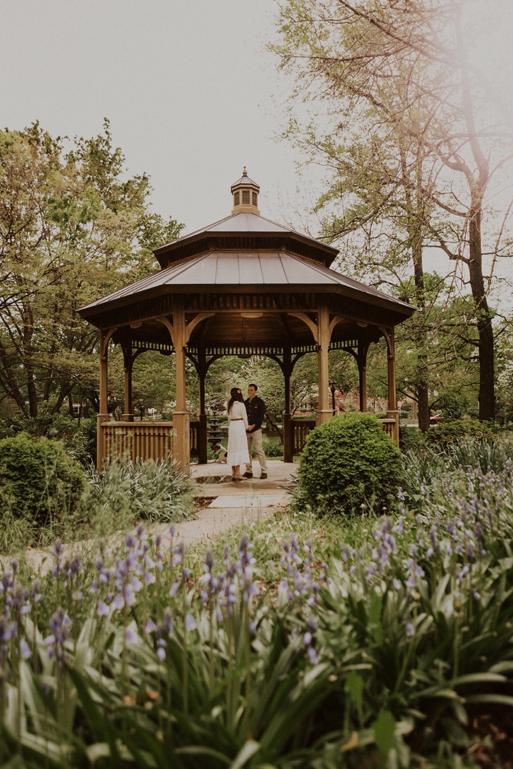 Couple holds hands standing in gazebo surrounded by spring flowers