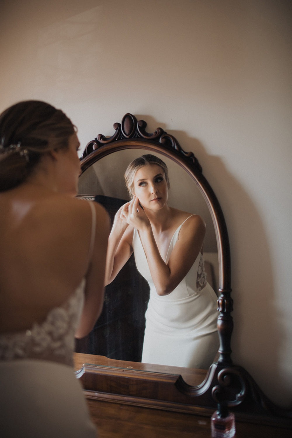 Bride looks into mirror as she puts on wedding earrings