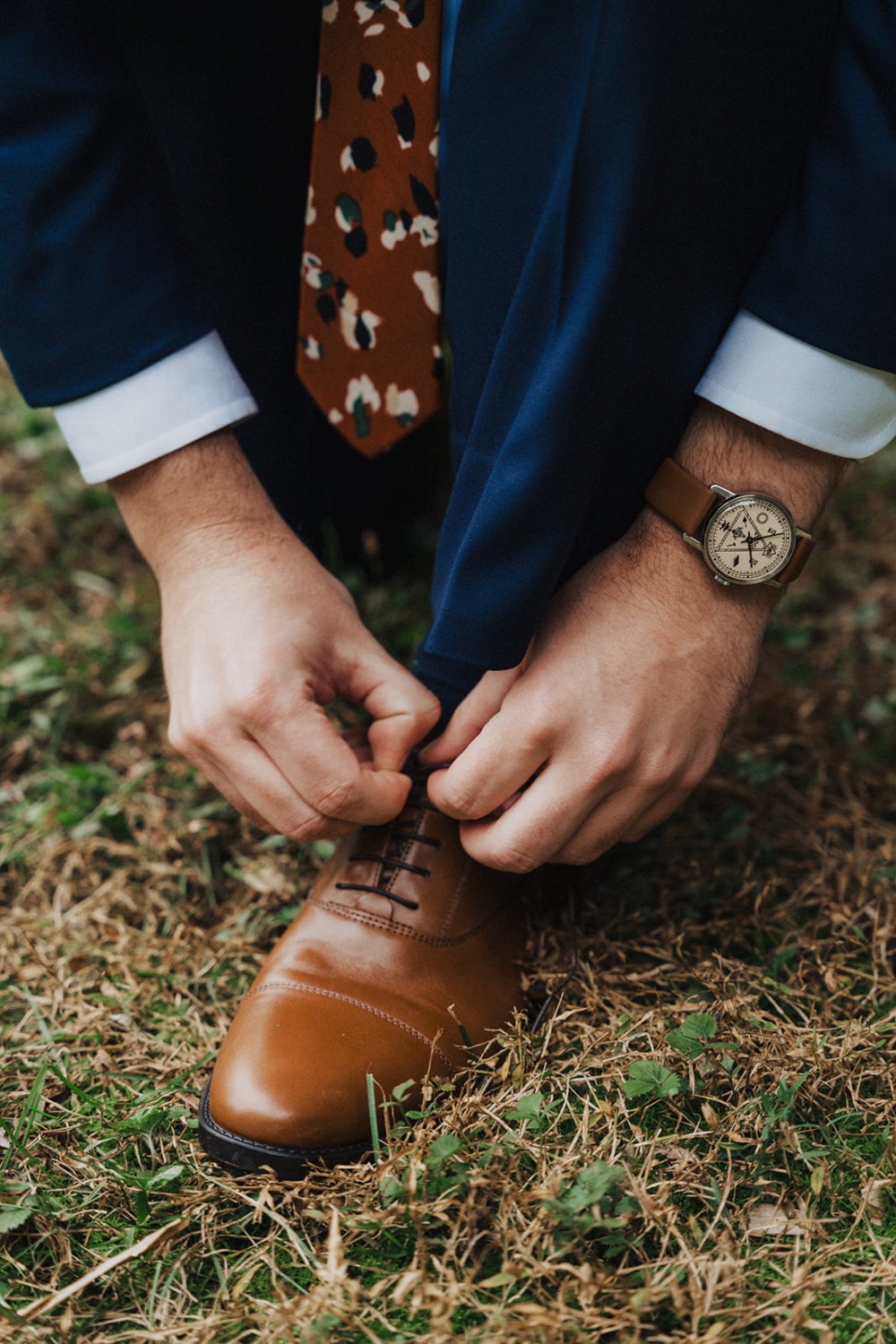 Groom ties shoelaces while getting ready at backyard wedding 