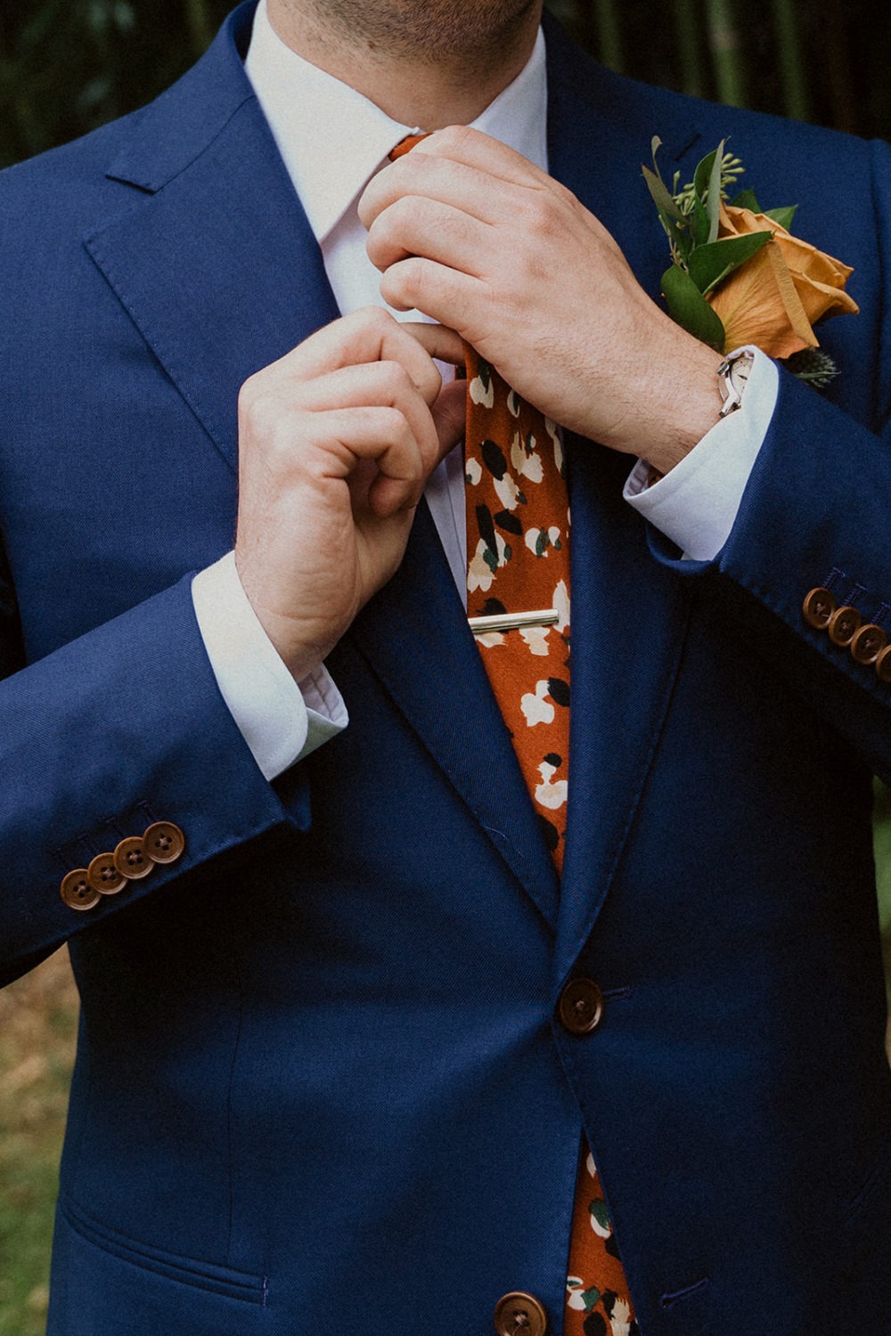 Groom ties tie while getting ready at backyard wedding 