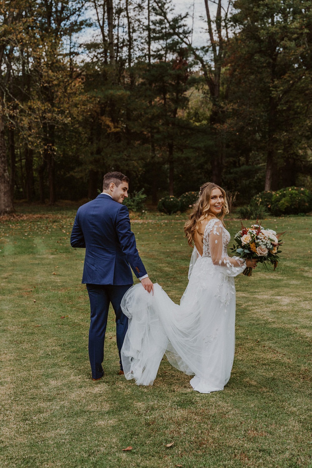 Groom holds bride's wedding dress train at Virginia woods wedding