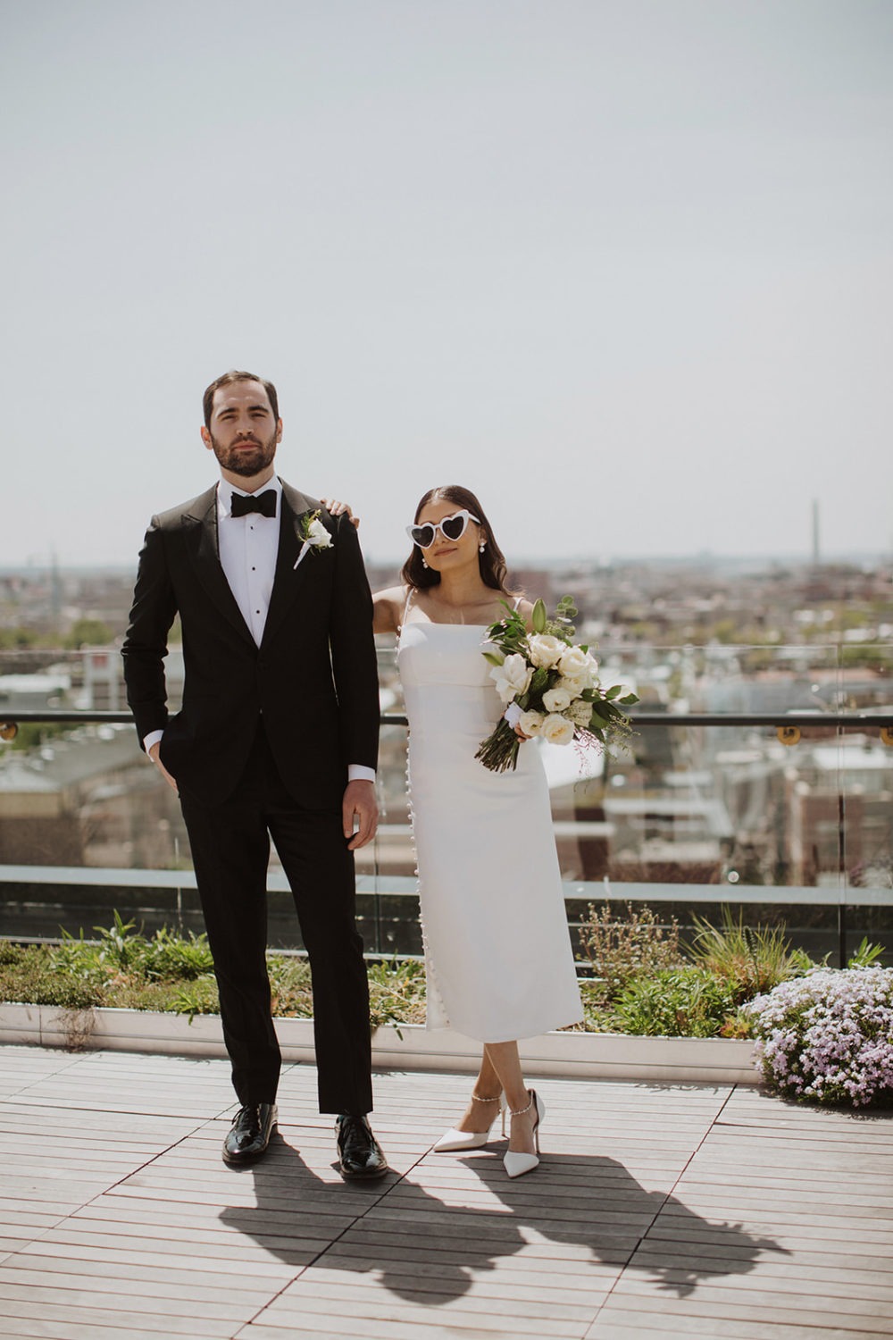 Couple poses with wedding bouquet and sunglasses at DC rooftop elopement