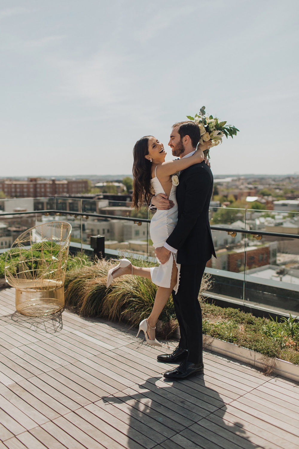 Groom picks up bride holding bouquet at DC rooftop elopement