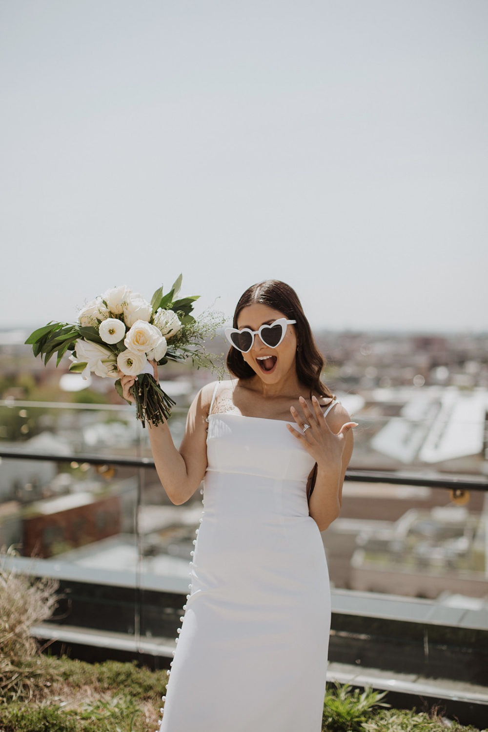 Bride shows of wedding band and wedding bouquet wearing sunglasses