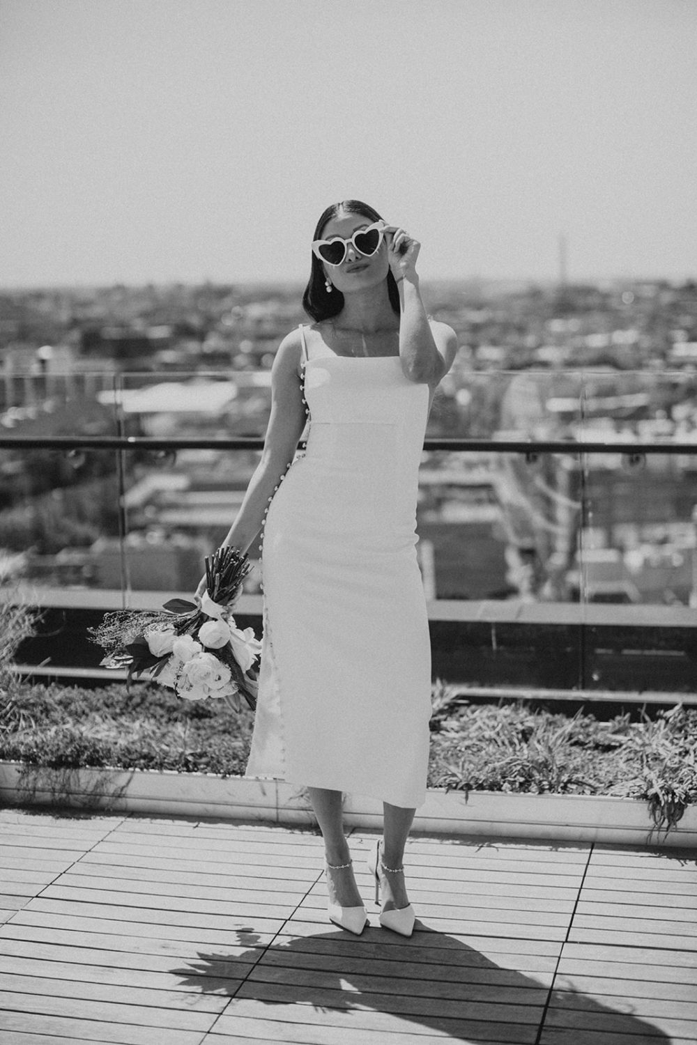 Bride holds wedding bouquet while wearing sunglasses on rooftop