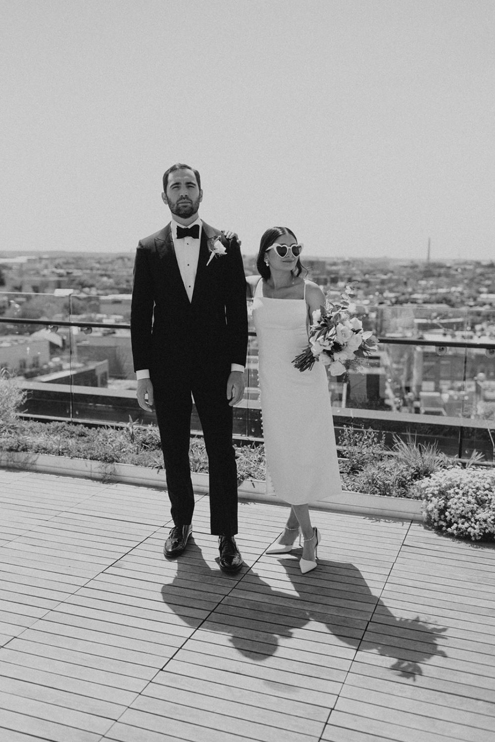Couple poses with wedding bouquet and sunglasses at DC rooftop elopement