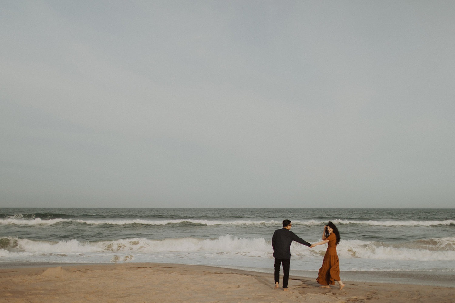 Couple walks holding hands at beach engagement session