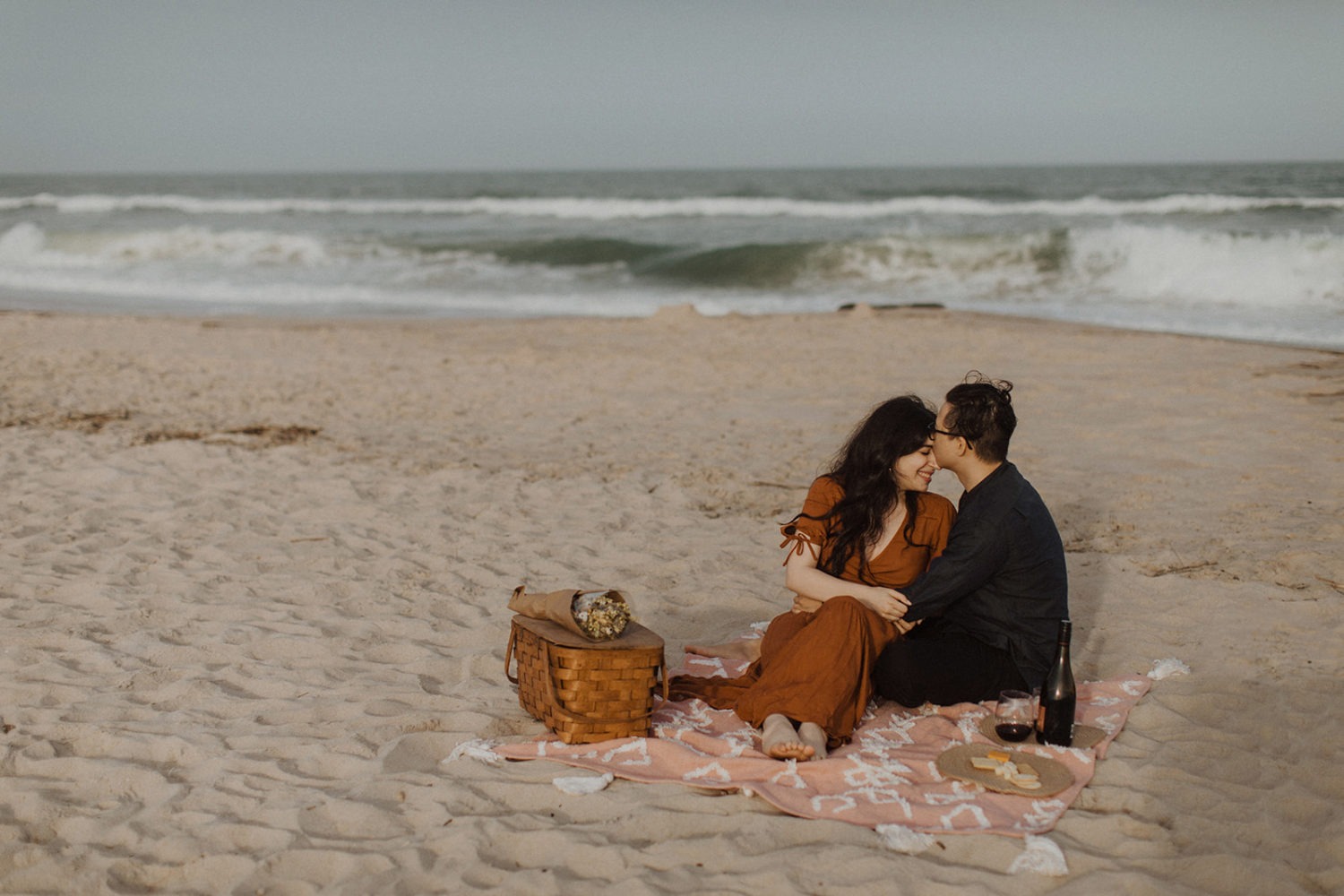 Couple seated embraces at beach engagement session