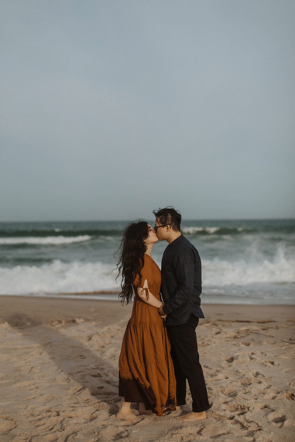 Couple kisses in front of ocean at beach engagement session