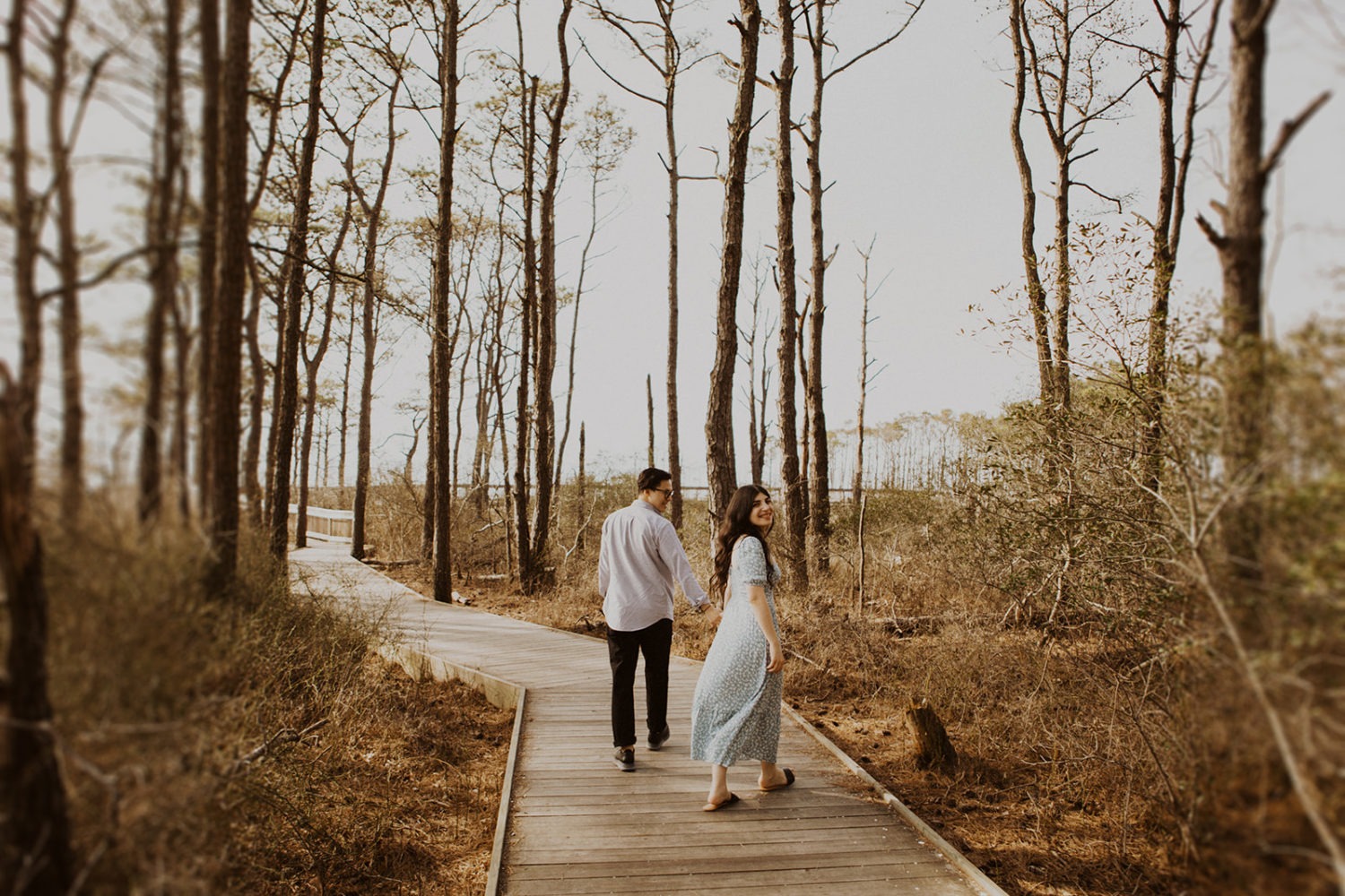 Couple holds hands while taking spring engagement photos in woods