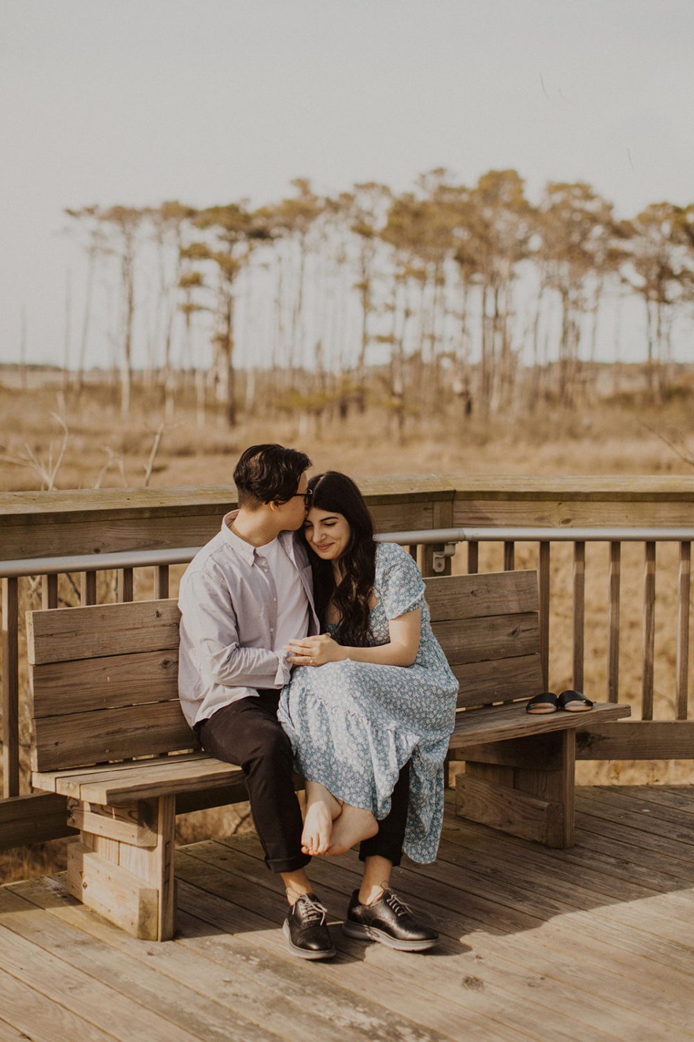 Couple snuggles while sitting on bench at Assateague Island engagement session