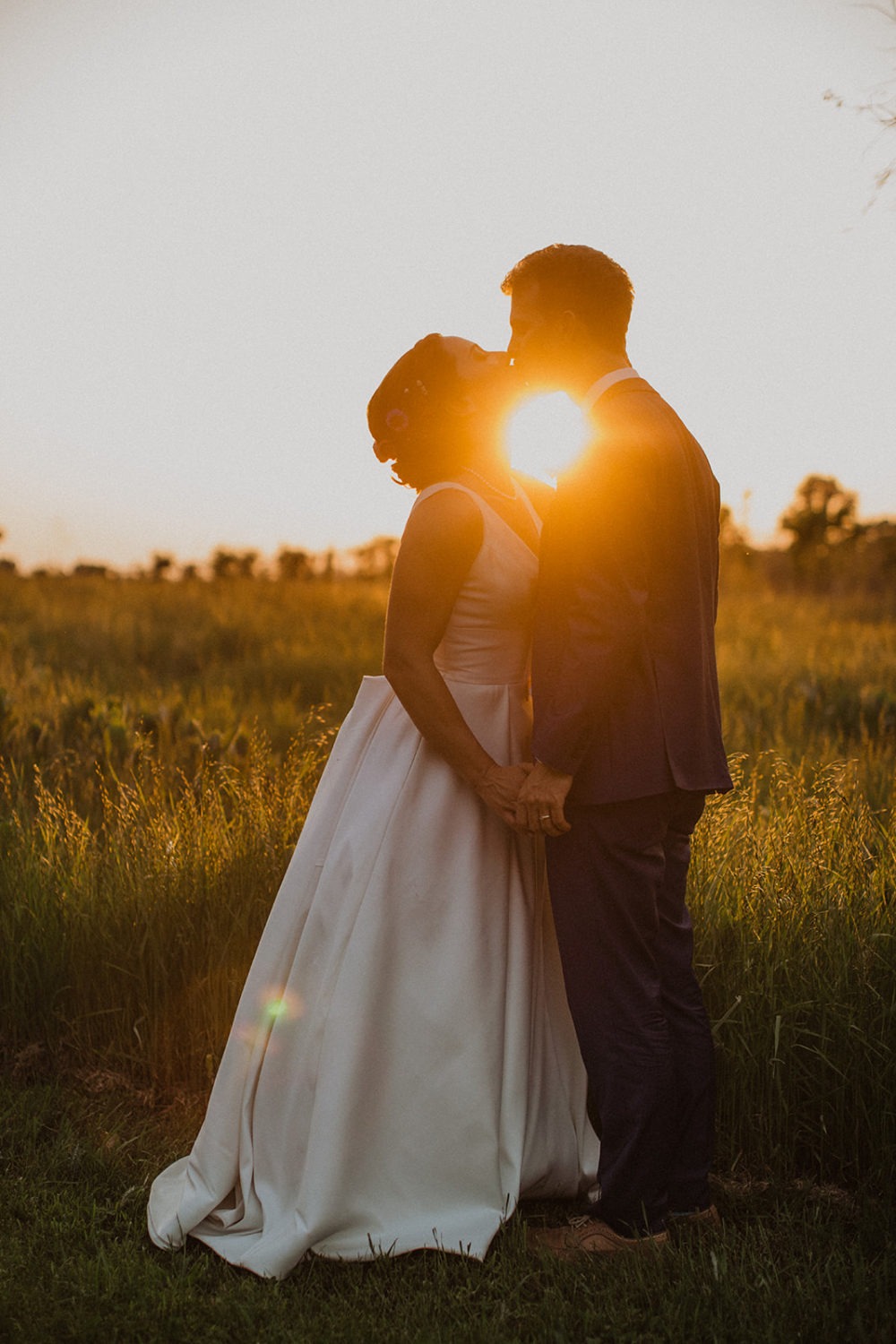 Couple kisses in a sunset field at nature wedding venue