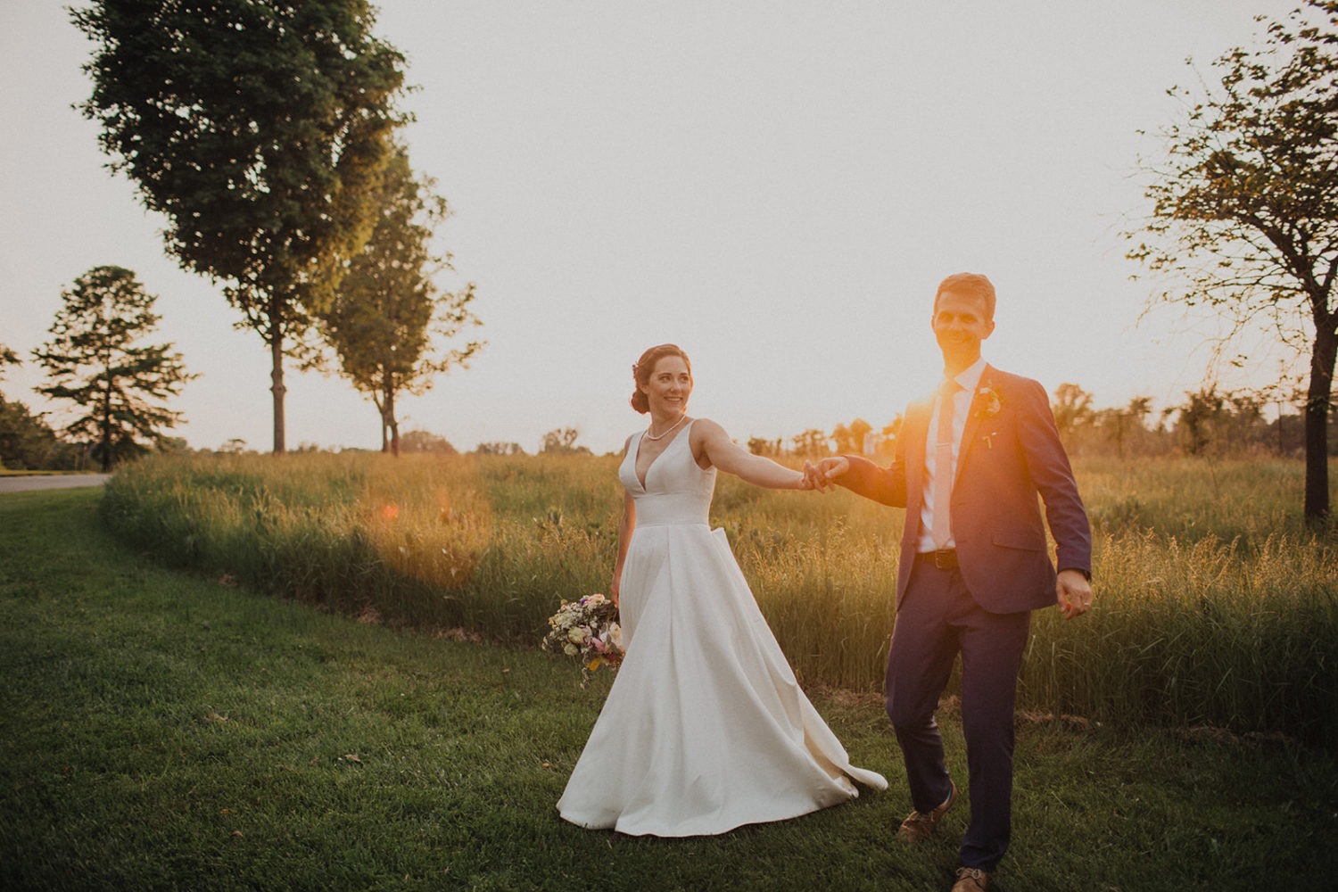 Couple holds hands in a sunset field at nature wedding venue