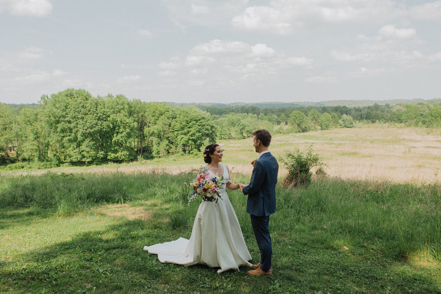 Couple holds hands on top of green grass hill at nature wedding venue