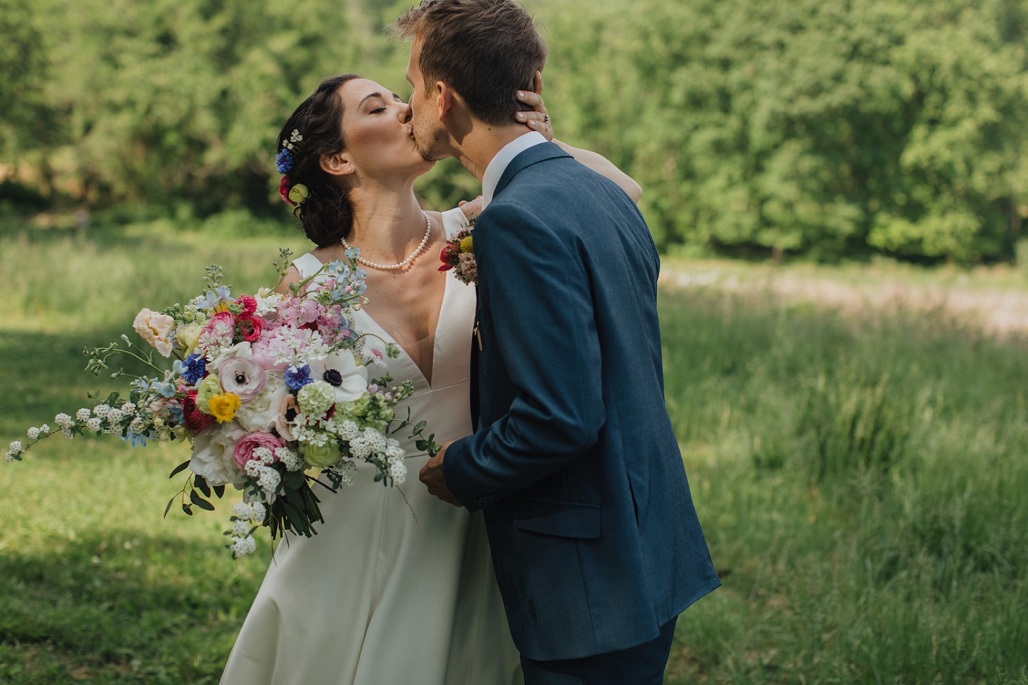 Couple kisses holding wedding bouquet at nature wedding venue