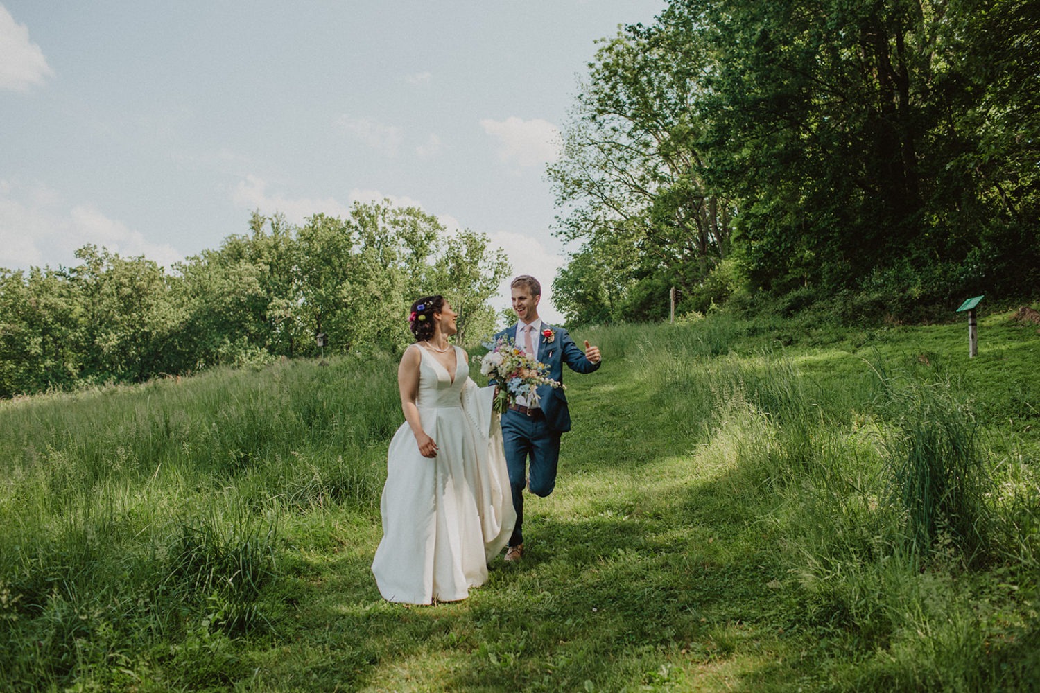 Couple runs down green-grass hill at nature center wedding