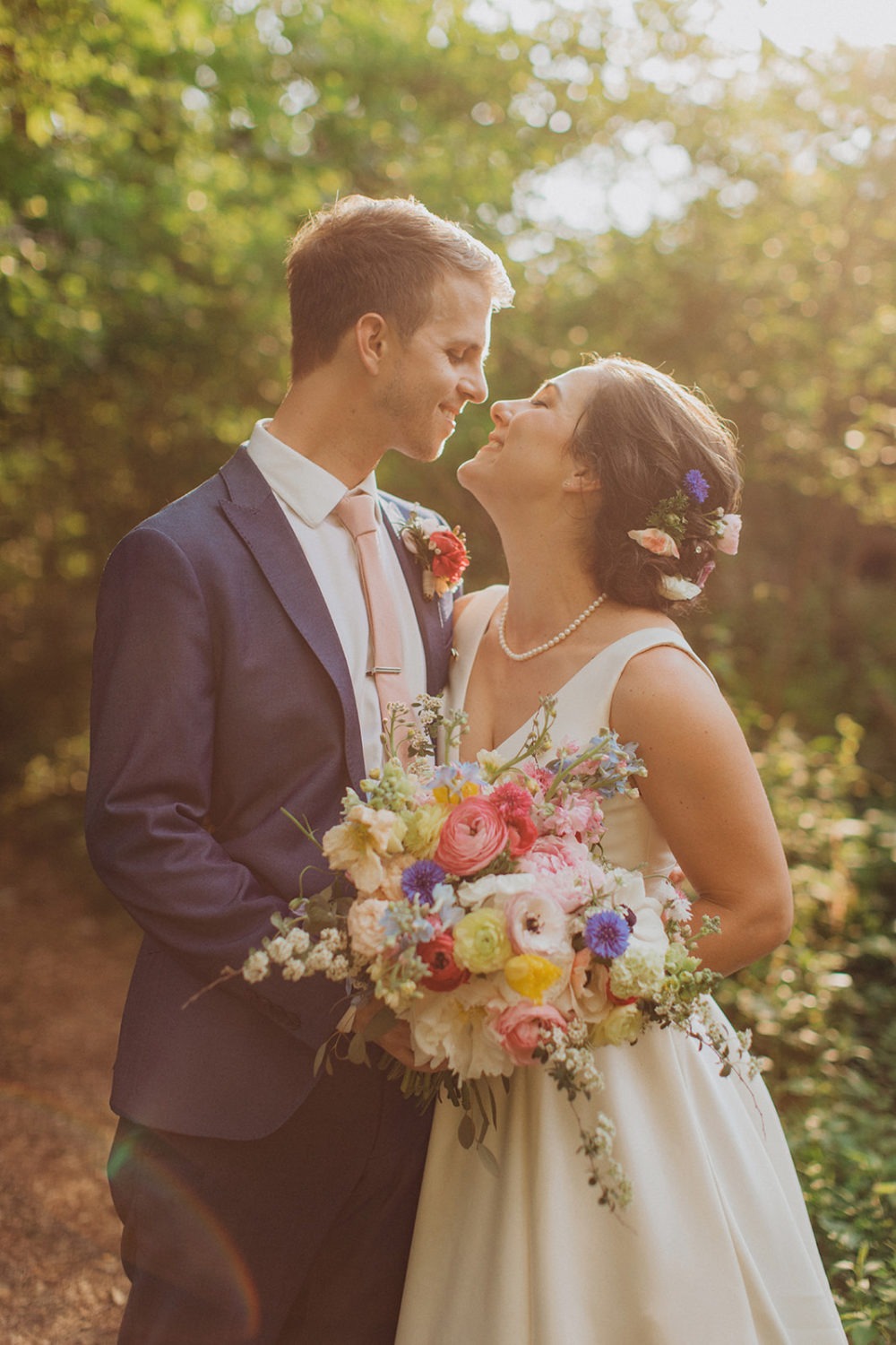 Couple smiles at each other in the sunlit woods of nature wedding venue