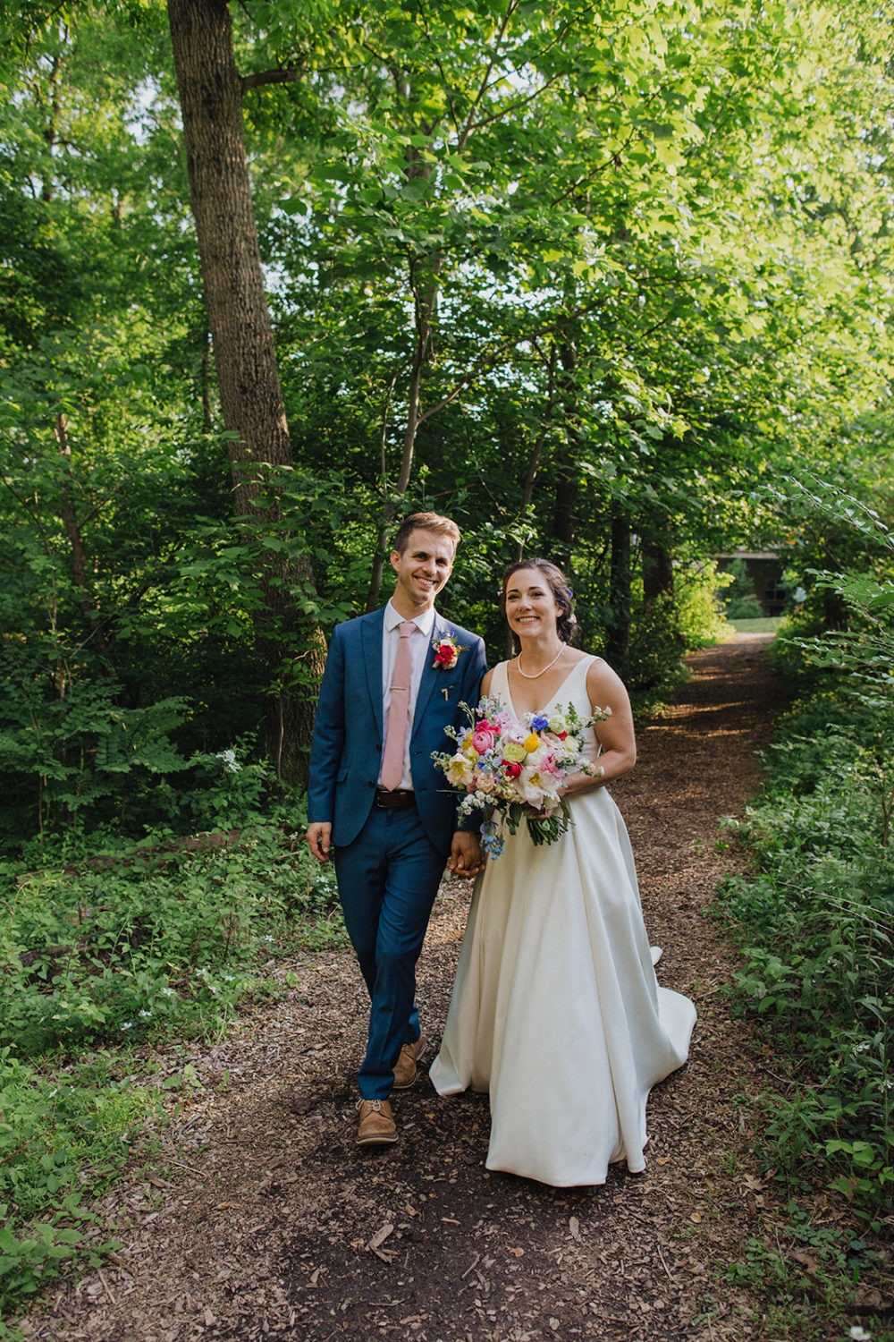 Couple walks through green woods at nature wedding venue