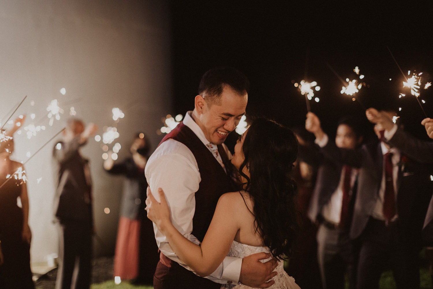 Couple embraces surrounded by sparklers at wedding exit