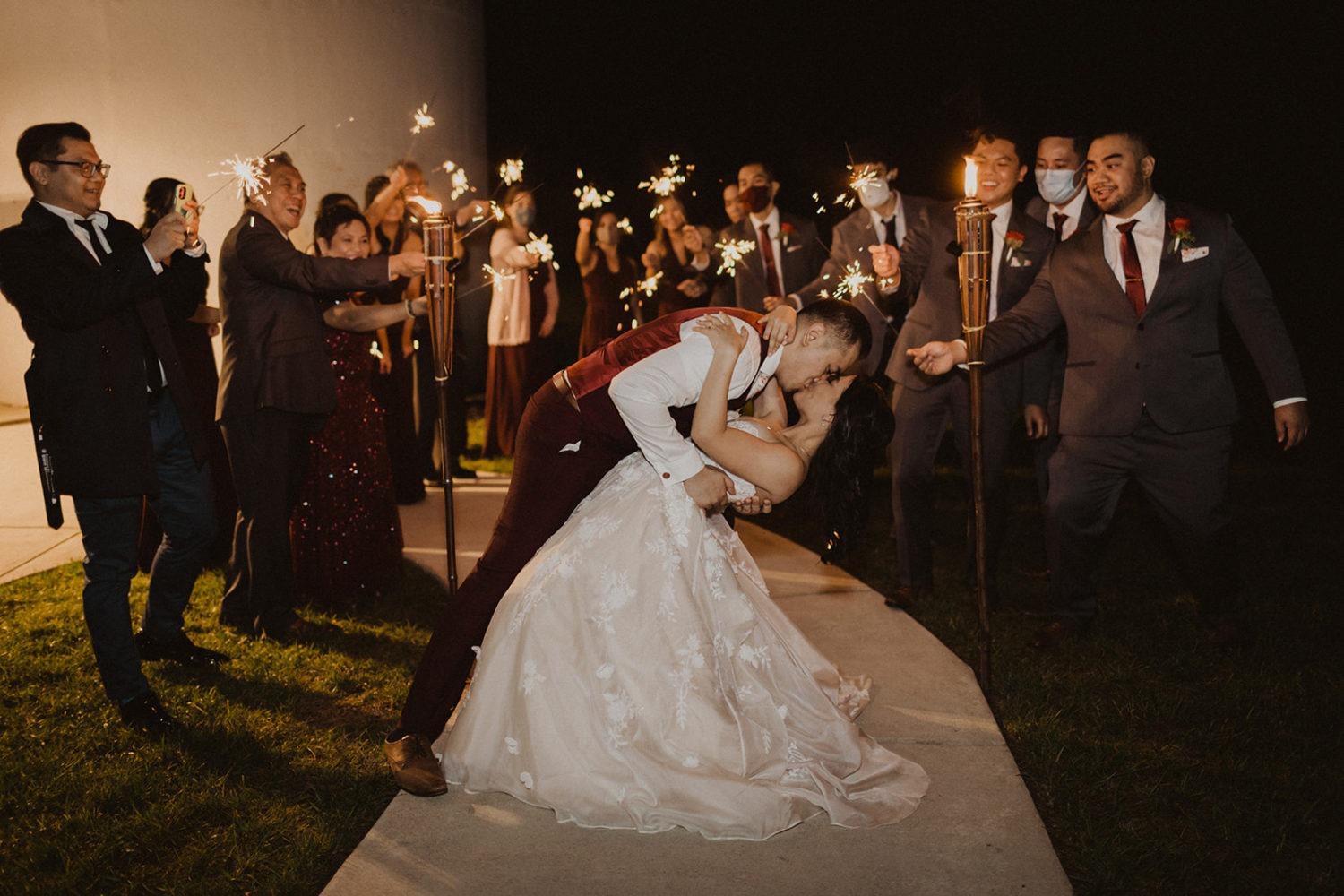 Couple kisses surrounded by sparklers at wedding exit