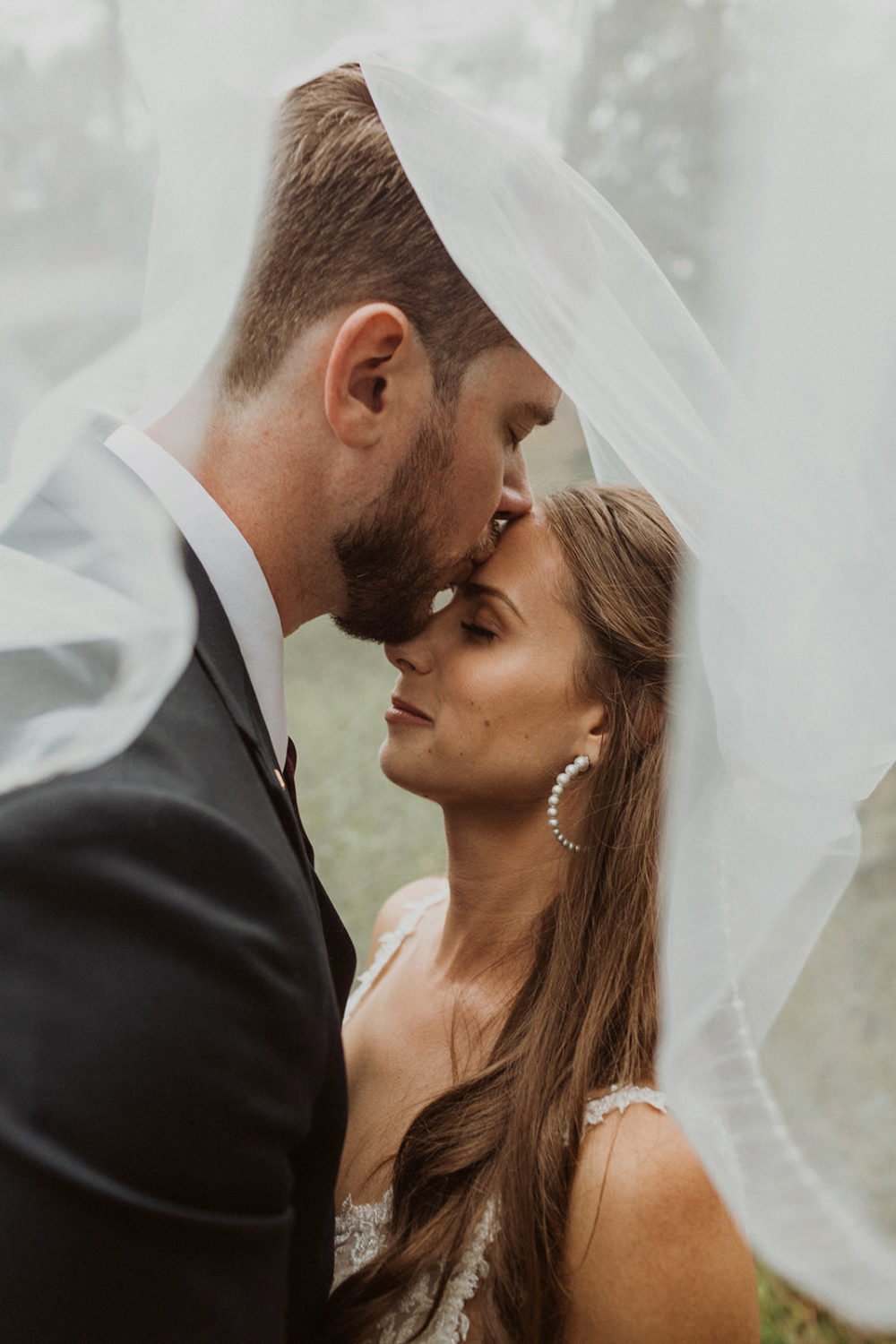 Couple kisses from underneath wedding veil