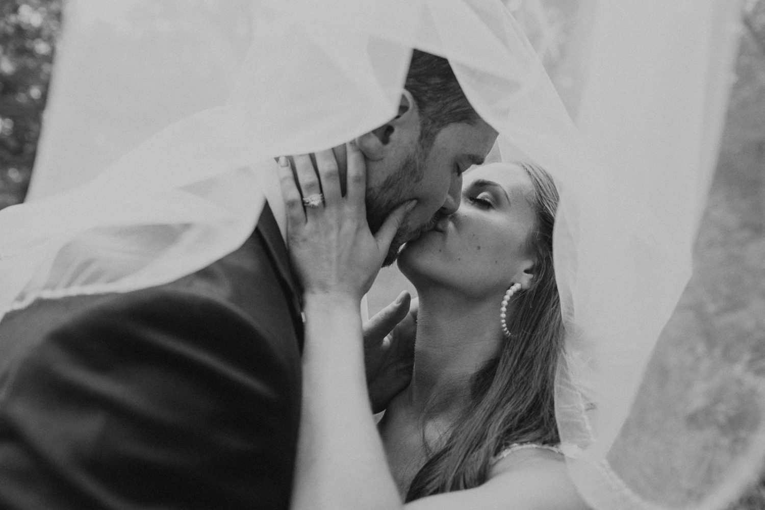 Couple kisses from underneath wedding veil