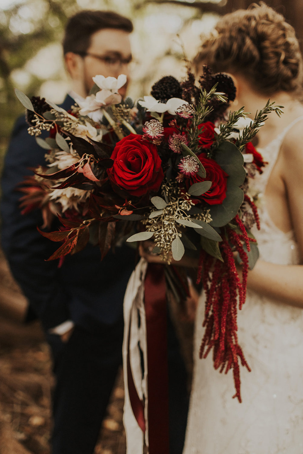 Bride holds red rose wedding bouquet at first look in woods